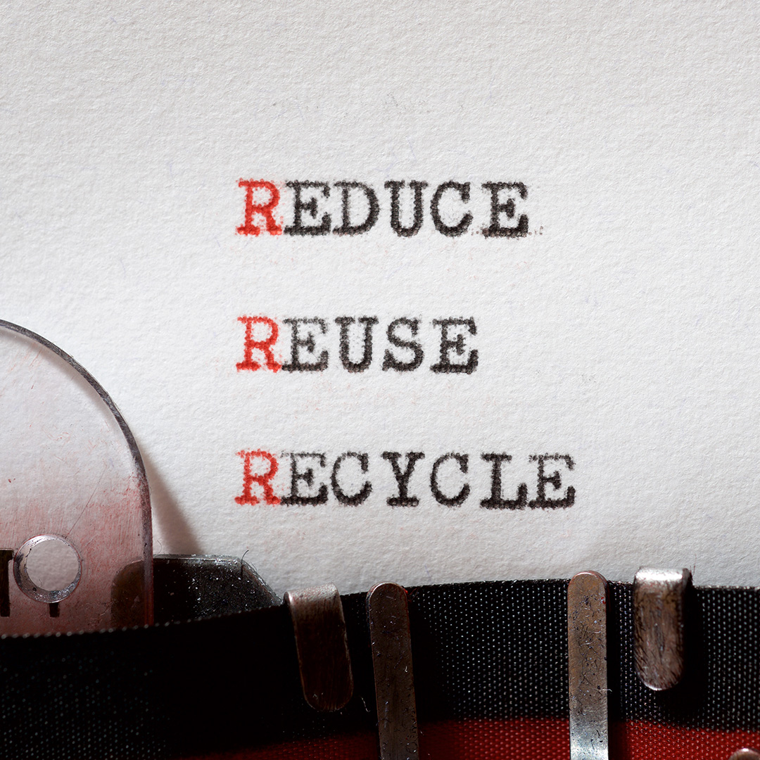 Vitt papper i skrivmaskin med orden Reduce, Reuse och Recycle i versaler där bokstaven R är röd.